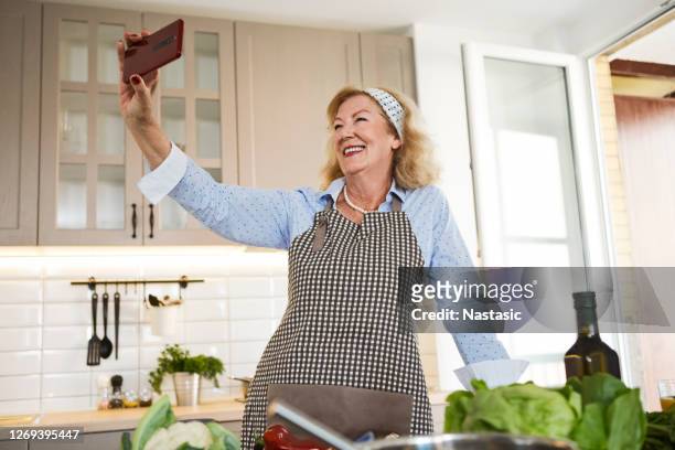 mature woman taking selfie in kitchen - old photographer imagens e fotografias de stock