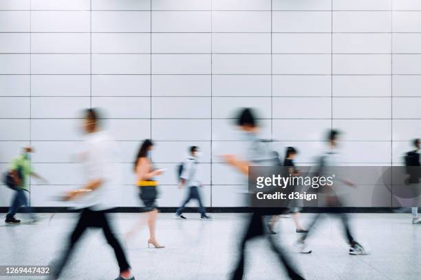 blurred motion of a crowd of busy commuters with protective face mask walking through platforms at subway station during office peak hours in the city - hauptverkehrszeit stock-fotos und bilder