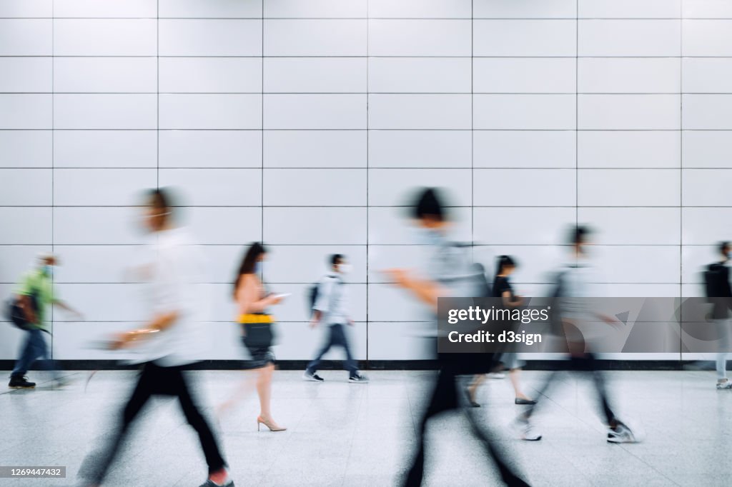 Blurred motion of a crowd of busy commuters with protective face mask walking through platforms at subway station during office peak hours in the city