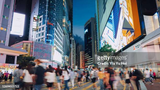 a typical city life in hong kong. blurred motion of a crowd of busy commuters crossing the street in downtown district during rush hour, against city buildings with illuminated and colourful billboards and commercial signs at night - causeway bay stockfoto's en -beelden
