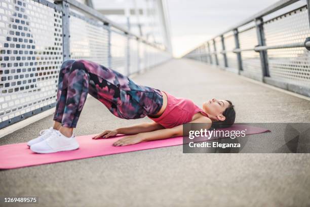 young sporty woman practicing yoga, doing dvi pada pithasana exercise, glute bridge pose, working out, wearing sportswear, outdoors - bridge imagens e fotografias de stock