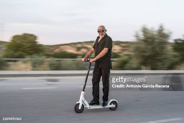 sweep photo of mature man driving an electric scooter, sweeping effect for green vehicle promotion - roller skate stock-fotos und bilder