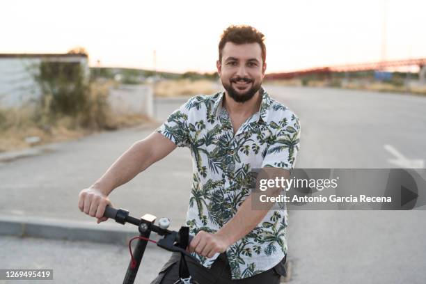 40-year-old man and hawaiian shirt looks smiling at camera with his scooter - 39 year old stock-fotos und bilder