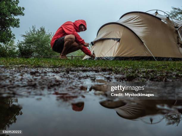 mann beim campen in einem regensturm erwischt - camping tent stock-fotos und bilder