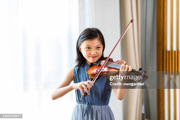 girl playing violin while standing by window at home - violin stock pictures, royalty-free photos & images