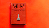 red book with text MLM Multi Level Marketing and a key on a red background
