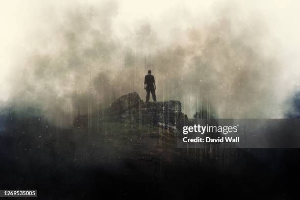 a man standing on top of a mountain. surrounded by clouds. with a grunge, dusty edit. - armageddon stock-fotos und bilder