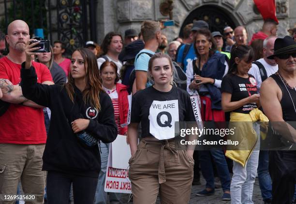 Mostly right-wing protesters, including a young woman wearing a QAnon shirt, observe riot police clearing Unter den Linden avenue during protests...