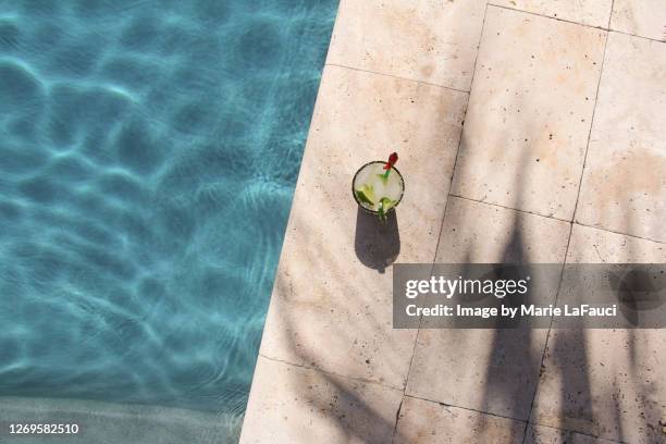 top angle view of a cocktail on the edge of a swimming pool - sunlight through drink glass stock-fotos und bilder