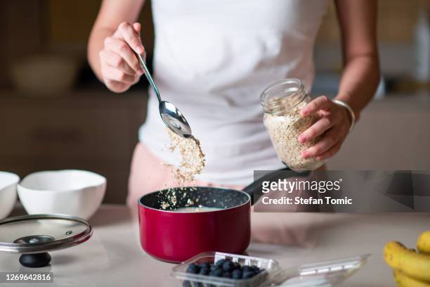 woman making morning breakfast oatmeal cereals and adding ingredients at home - oatmeal stock pictures, royalty-free photos & images
