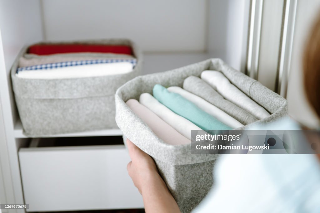 Mulher organizando roupas no guarda-roupa, colocando camisas em caixas, cestas em prateleiras. Roupas bem dobradas após a lavanderia. Conceito de estilo de vida minimalista