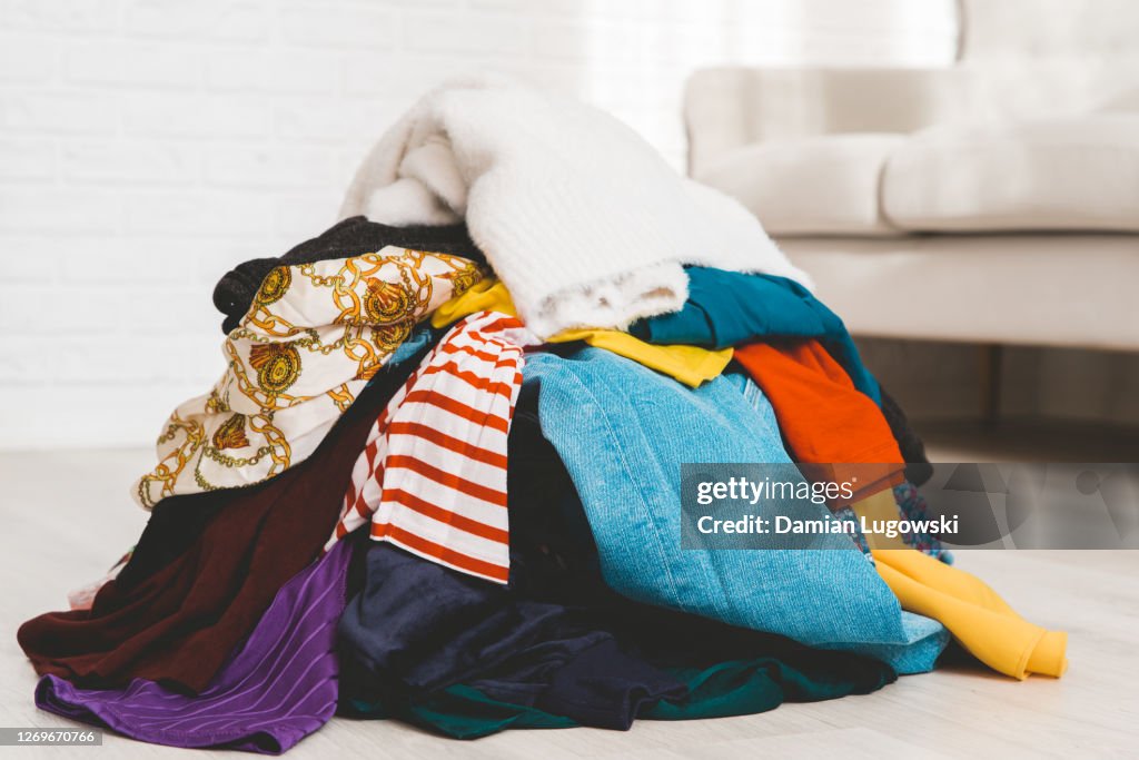 Pile of unfolded clothes for laundry on the floor. Heap of used clothes for donation or recycling. Decluttering concept