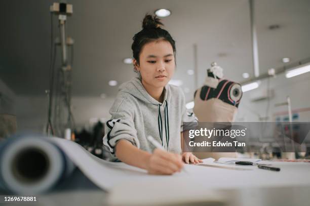 asian chinese female fashion college student writing down measurement doing clothing project at college workshop