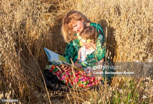 een meisje leest een boek aan haar kind, meisjes 5 jaar oud. een familie van kaukasiërs zit op een havergebied bij zonsondergang. familie vakantie. - 40 44 years woman caucasian stockfoto's en -beelden