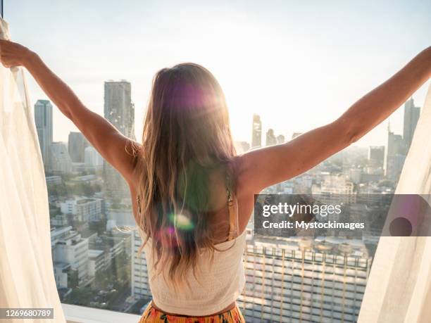 kvinna öppnar gardiner på hotellrum vid soluppgången - open city bildbanksfoton och bilder