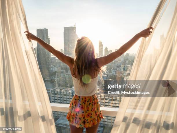 woman opens curtains in bedroom room at sunrise - morning stock pictures, royalty-free photos & images