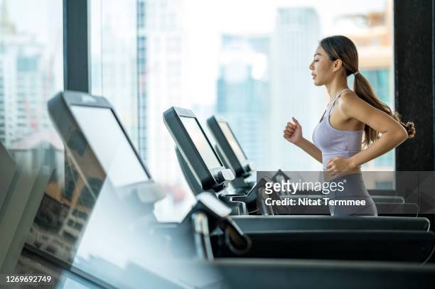 side view of young asian women athlete running or jogging on treadmill in a hotel sport club. - asian woman fitness stockfoto's en -beelden