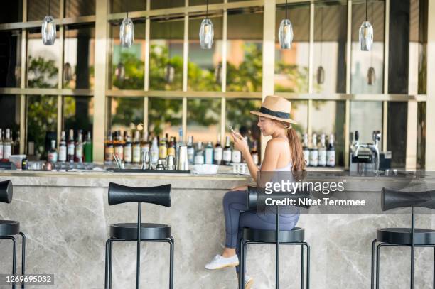 asian women tourist ordering drink and text messaging in luxury hotel bar counter. - hotel bar stock pictures, royalty-free photos & images
