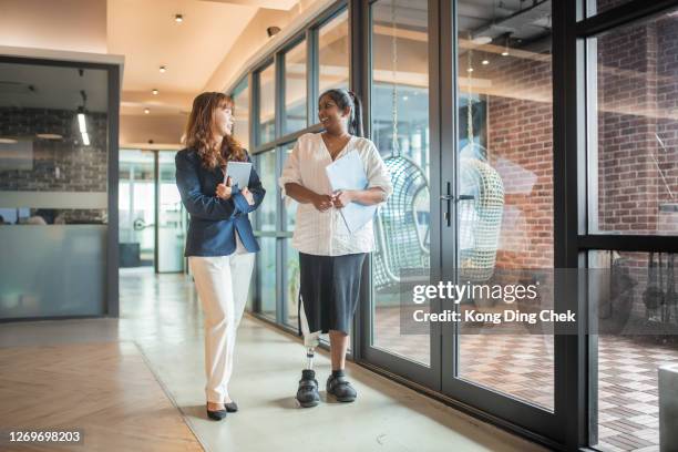 azië indische vrouwelijke gehandicapte zakenvrouwen met prothetische lidmaat die document houden en bij de bureaugang lopen. ze is in gesprek met haar collega - amputatie stockfoto's en -beelden