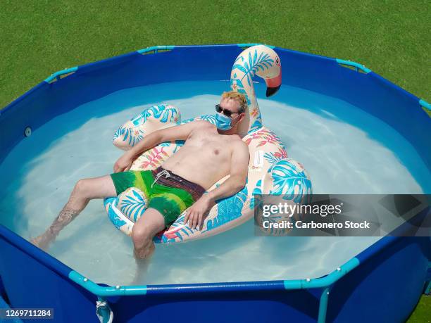 adult man wears a protective mask as he relaxes in the pool in summer - luftmatratze von oben stock-fotos und bilder