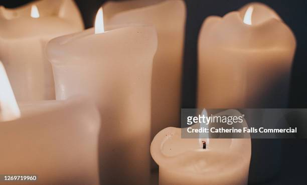 group of lit white candles flickering in the darkness - mourning candles stock pictures, royalty-free photos & images