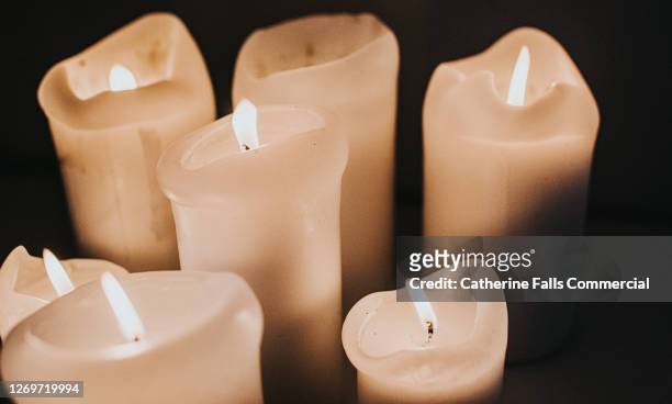group of lit white candles flickering in the darkness - mourning candles stock pictures, royalty-free photos & images