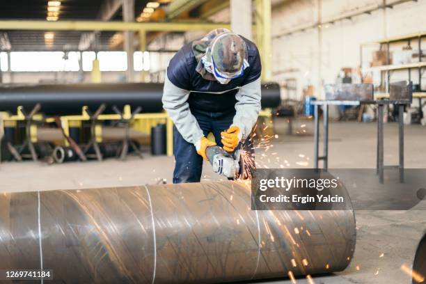 de arbeider van het metaal in beschermend kostuum en handschoenen snijdende pijp met elektrische molen in fabriek - slijptol stockfoto's en -beelden