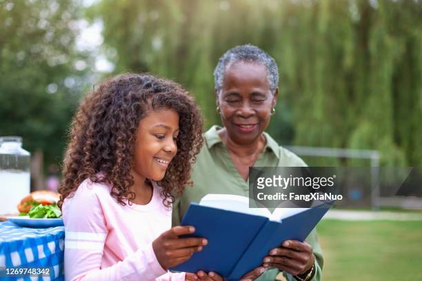 granddaughter reading book with grandmother at public park picnic - history stock pictures, royalty-free photos & images