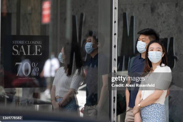 People wearing masks wait in line near a 'store closing sale' sign at Neiman Marcus in Hudson Yards as the city continues Phase 4 of re-opening...