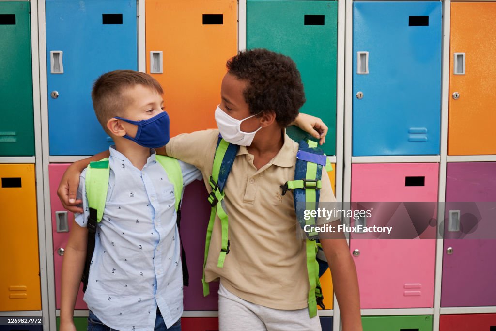 Happy multi ethnic male friends hugging while wearing protective face mask in the school