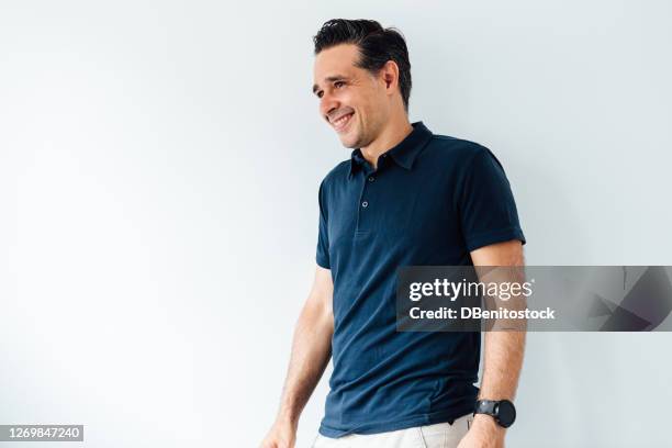 young entrepreneur man smiling with blue polo shirt and beige pants on white background - polo shirt stock pictures, royalty-free photos & images