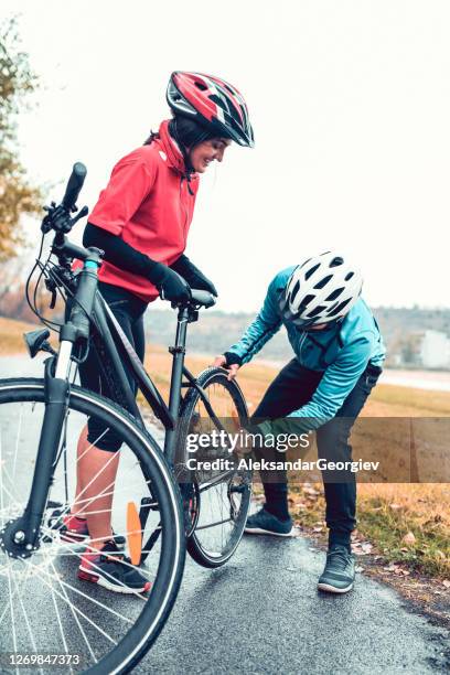 male fixing girlfriend's bike wheel while cycling together - bike tyre stock pictures, royalty-free photos & images