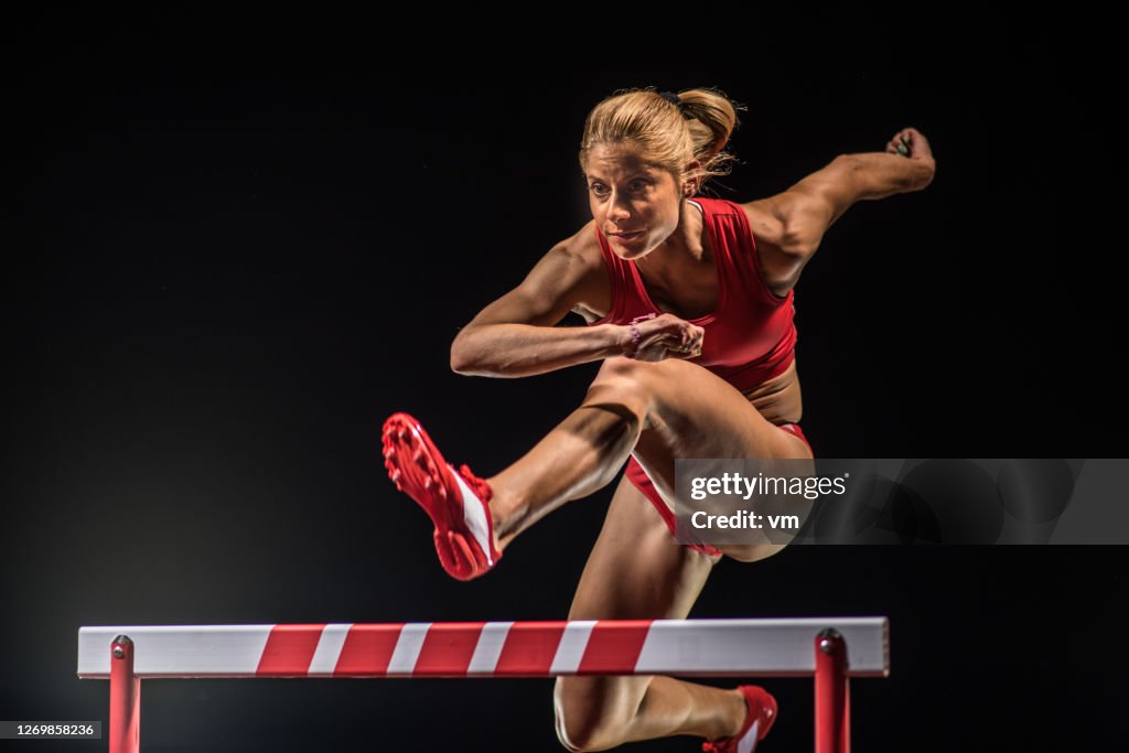 Caucasian female athlete jumping over a hurdle