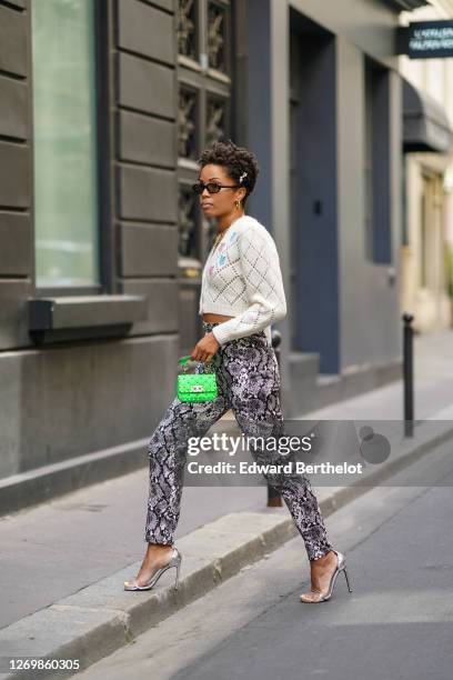 Ellie Delphine wears pearl beaded hair pins, golden earrings, a golden chain necklace, a white wool floral print cropped cardigan from Alessandra...