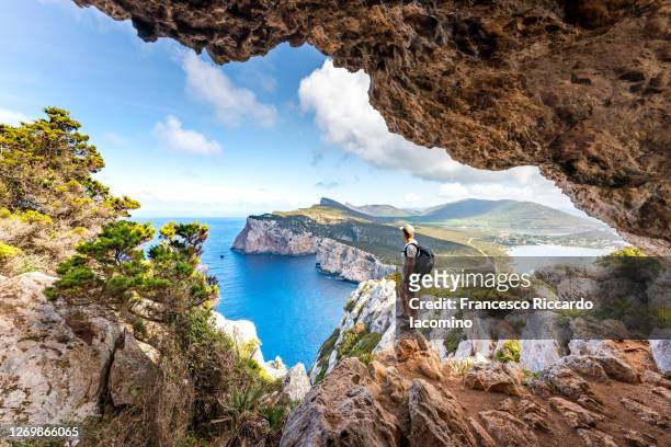 capo caccia, hiker admiring the view from a cave. sardinia, italy - avventura foto e immagini stock