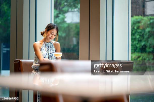 young asian women tourist sits at hotel bar and has a drink. business travel, vacation. - asian luxury lifestyle foto e immagini stock