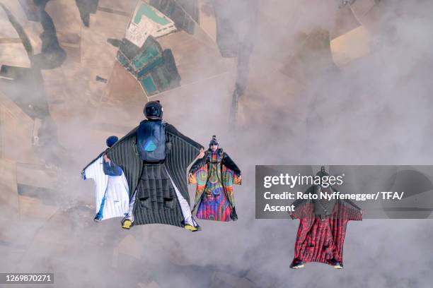 wingsuit fliers soar in formation above rural landscape - wing suit stock pictures, royalty-free photos & images