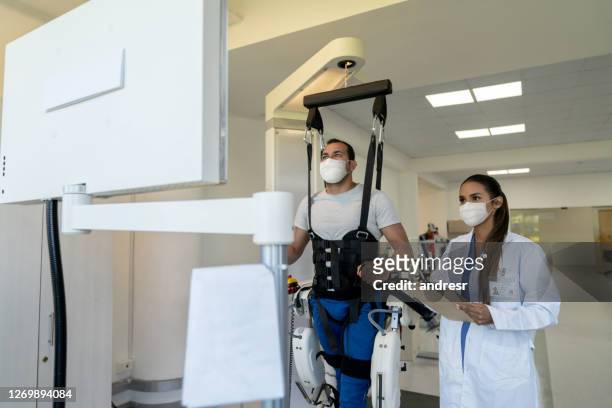 patient doing physiotherapy with an exoskeleton with his physical therapist supervising and both wearing facemasks - woman leg spread stock pictures, royalty-free photos & images
