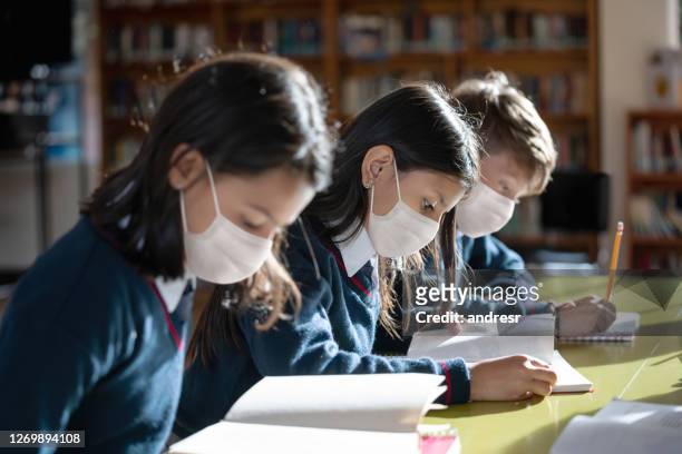group of kids studying at the school wearing facemasks - biosecurity stock pictures, royalty-free photos & images