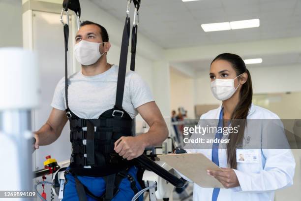 patient doing physical therapy with an exoskeleton with his physical therapist supervising and both wearing facemasks - woman leg spread stock pictures, royalty-free photos & images