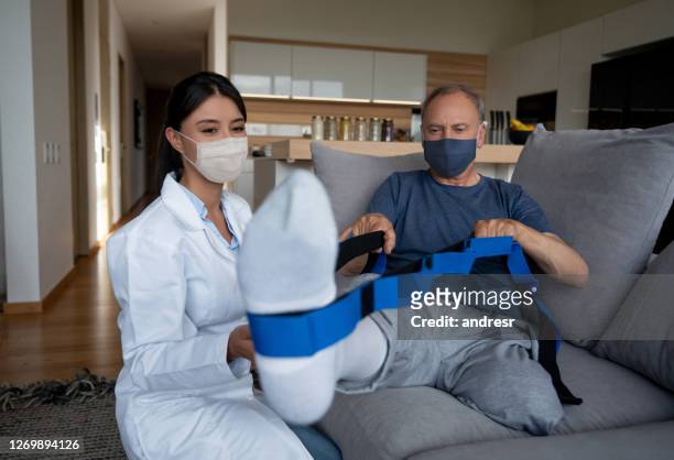physical therapist helping a disabled man at home with his physiotherapy and wearing facemasks - amputee rehab stock pictures, royalty-free photos & images