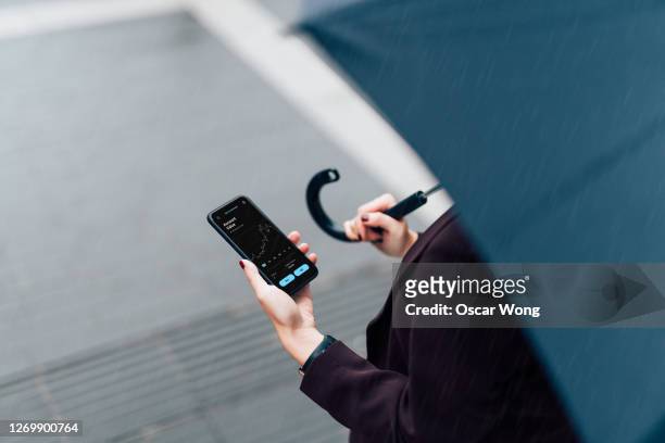 businesswoman with umbrella, checking stock market on smart phone in the rain - pre game stockfoto's en -beelden