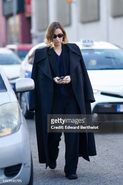 Guest wears sunglasses, a black wool long coat, a black jacket, a blue pullover, suit pants, shoes, outside Marni, during Milan Fashion Week...