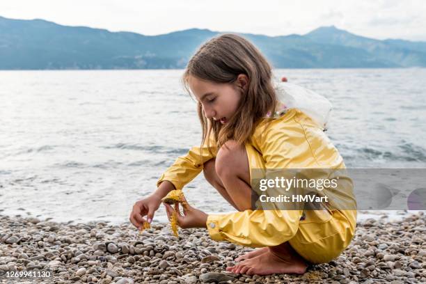 barefoot girl in yellow rain coat exploring the beach after summer storm - picking up child stock pictures, royalty-free photos & images