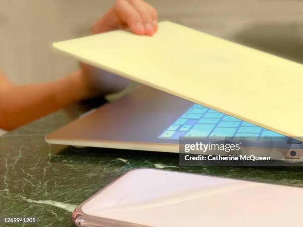 mixed-race female closes laptop while working at kitchen counter - closing laptop stock pictures, royalty-free photos & images