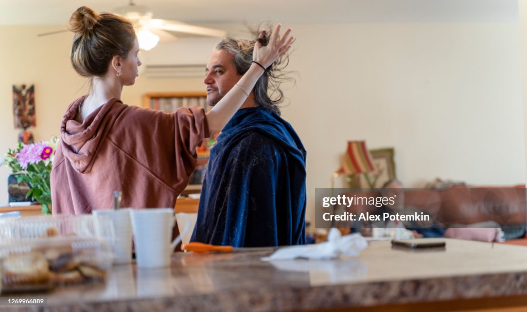 Do It Yourself - home haircut. Late teenage girl, a daughter, gives a haircut to her father, mature 50-years-old man with long hair.