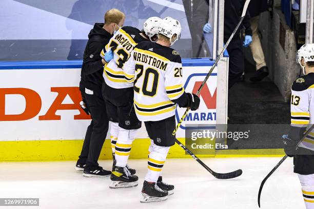 Charlie McAvoy of the Boston Bruins is assisted off the ice by the trainer and Joakim Nordstrom after being hit by Cedric Paquette of the Tampa Bay...