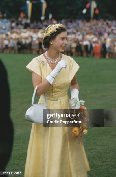 Queen Elizabeth II holds a bouquet of flowers as she waves to crowds attending a school children's rally at Manuka Park in Canberra during the royal...