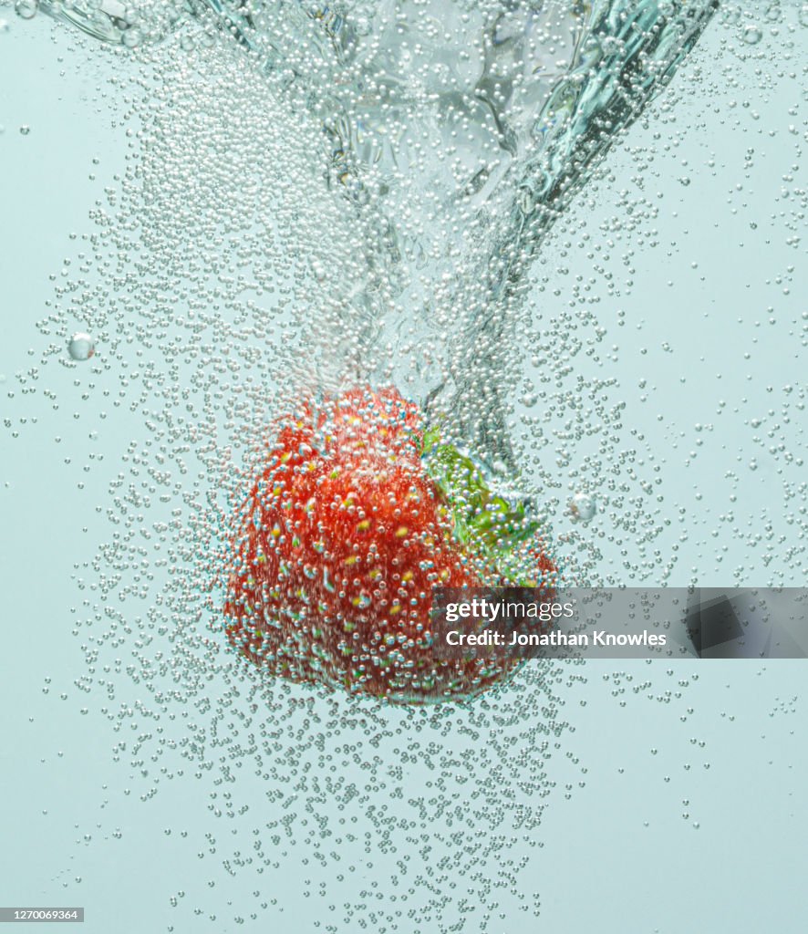 Strawberry falling in fizzy water