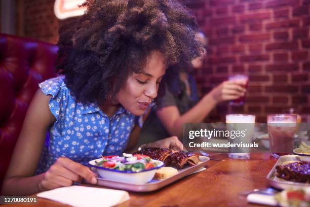 close-up of african-american woman enjoying and smelling bbq ribs in retro restaurant with friends - portugal food stock pictures, royalty-free photos & images